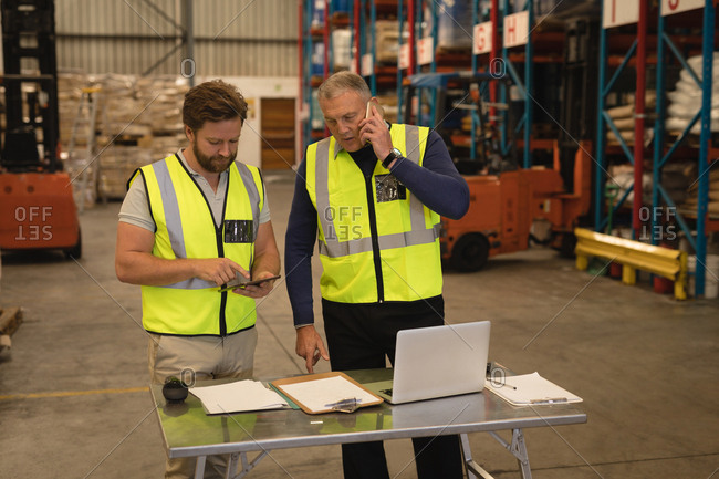 Male supervisors talking on mobile phone and using digital tablet in warehouse