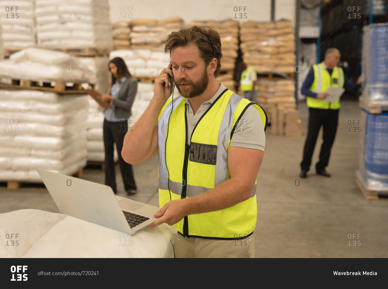 Male supervisor talking on mobile phone while using laptop in warehouse