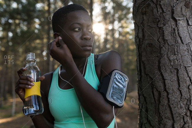 Female athlete with water bottle listening to music in the forest