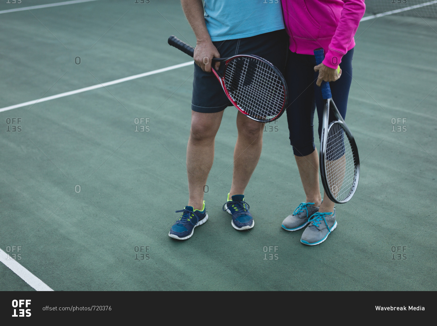 Low section of senior couple standing in tennis court