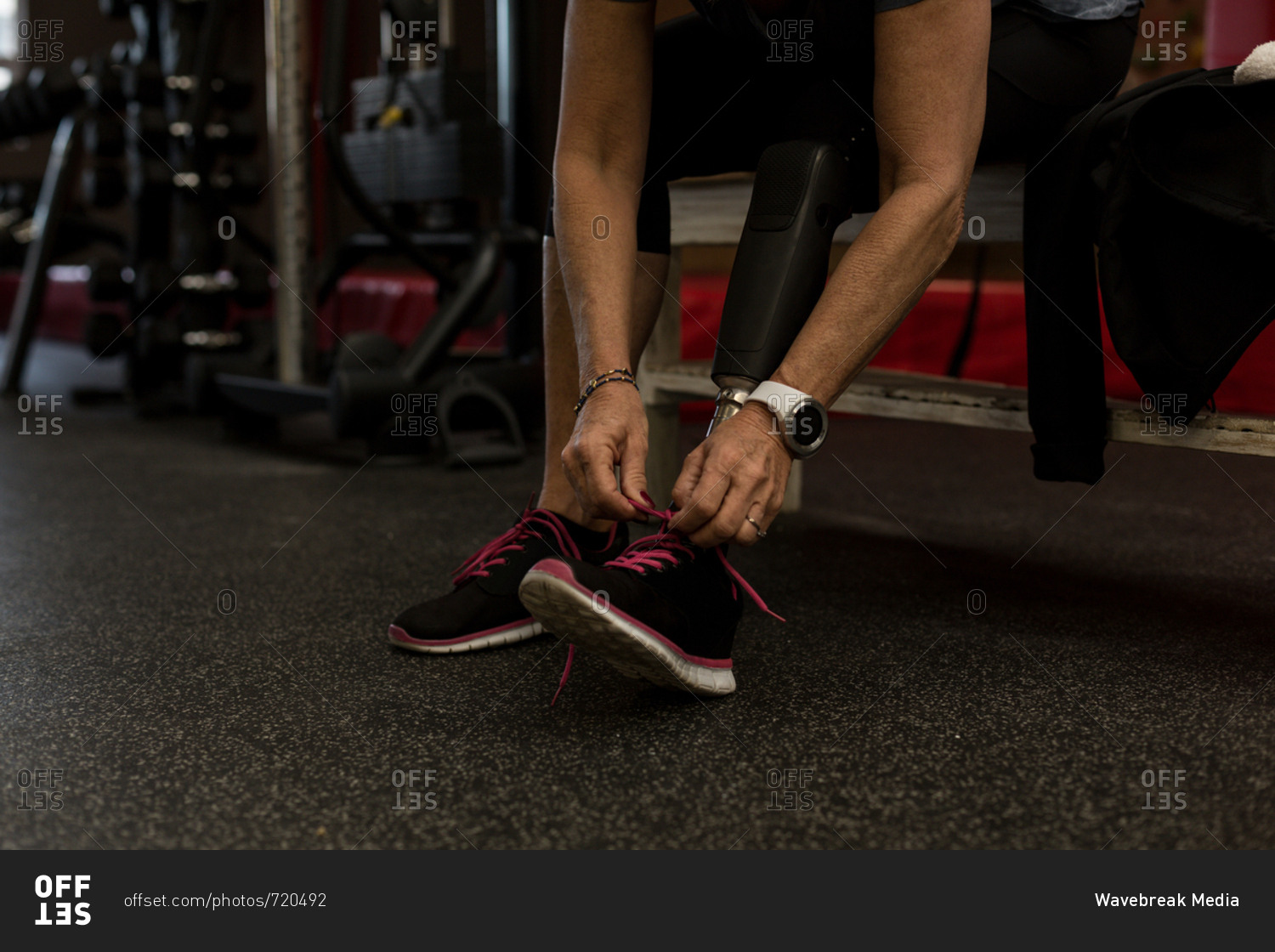 Low section of disabled woman tying shoelaces in gym
