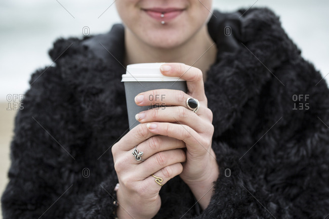 Close up of young woman wearing black furry jacket holding paper cup with hot drink
