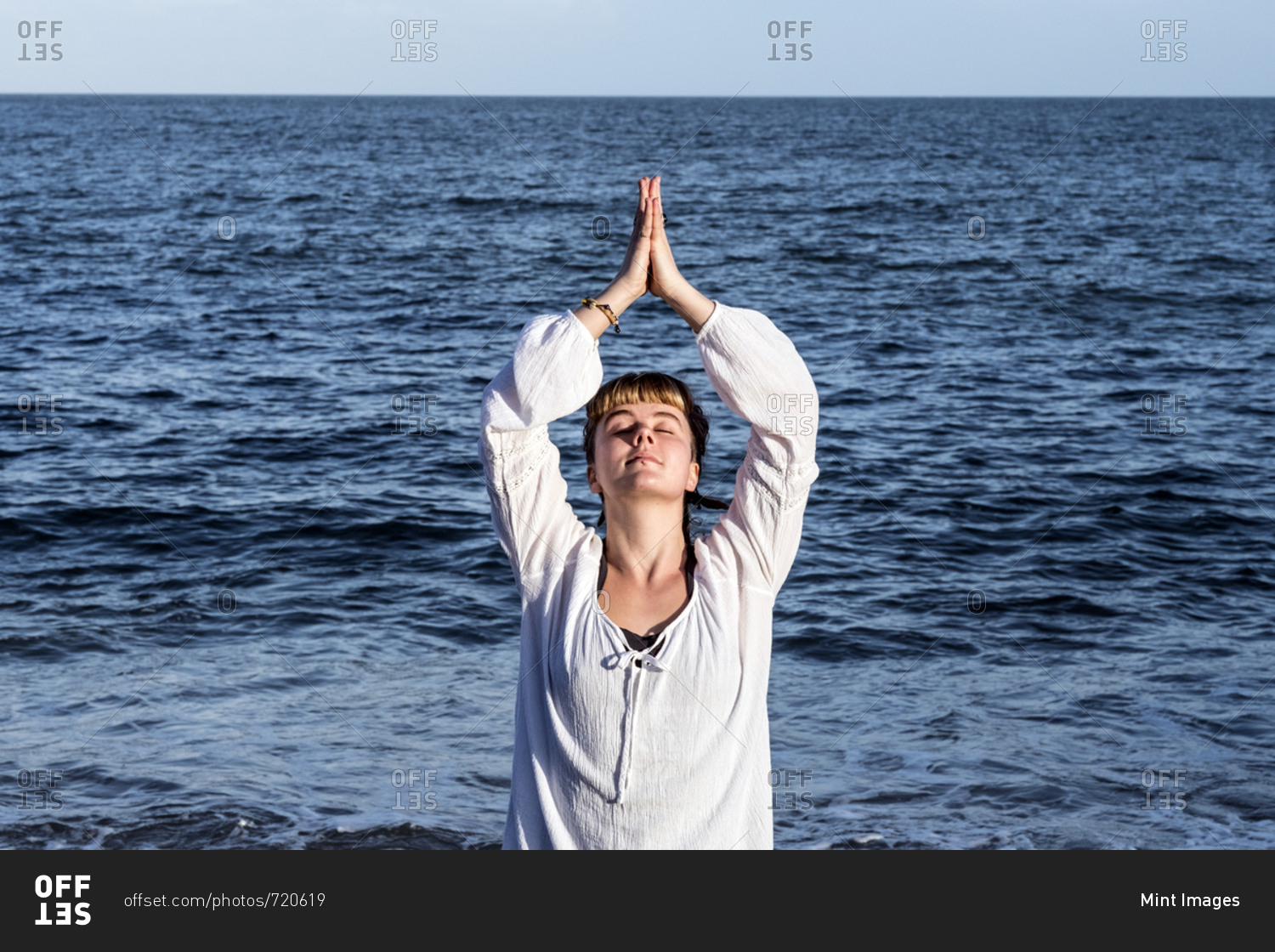 Young woman with brown hair wearing white blouse standing on a beach by the ocean, doing Tai Chi
