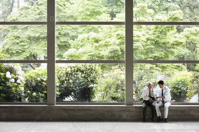 Two businessmen working on a notebook computer and sitting in front of a large window in the lobby of a convention centre