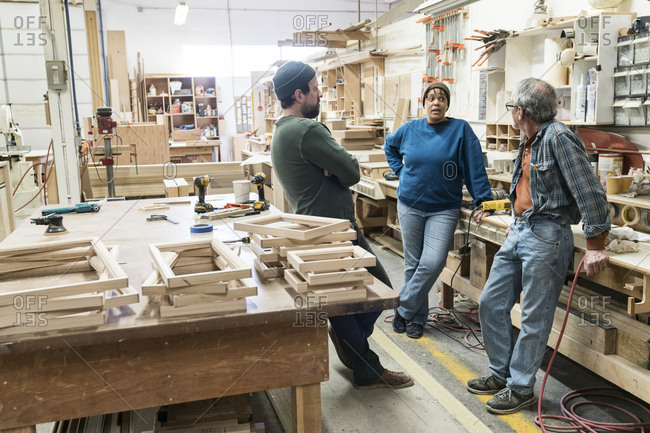 A group of mixed race carpenters discussing a project at a work station in a large woodworking shop
