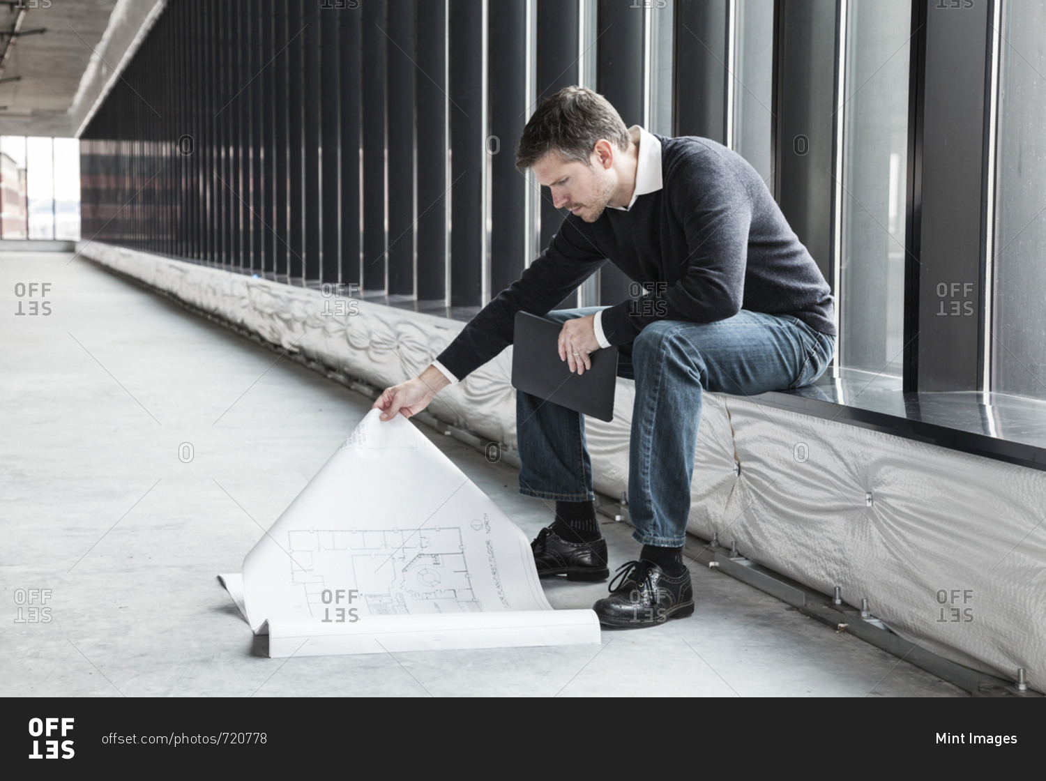 A Caucasian male architect working on building plans in a new raw business space