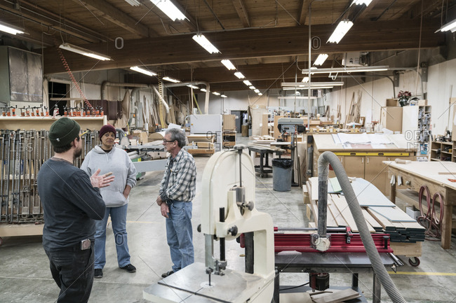 A group of mixed race carpenters discussing a project at a work station in a large woodworking shop
