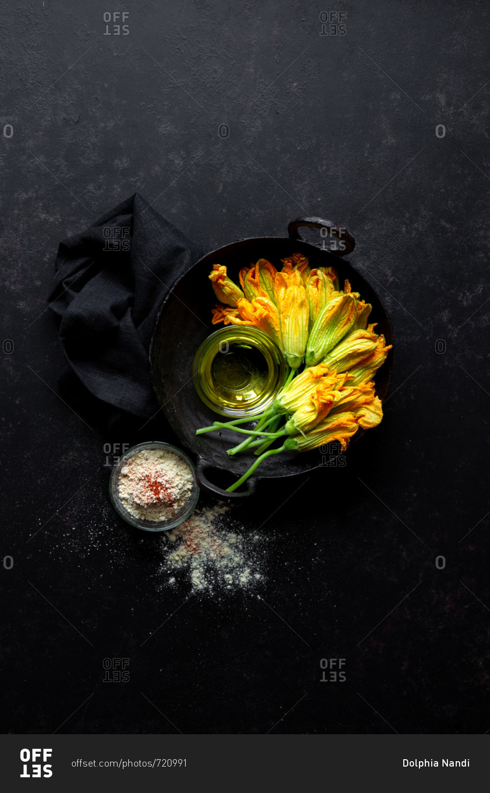Bunch of fresh squash blossoms with vegetable oil and gluten-free chickpea flour on rustic dark background