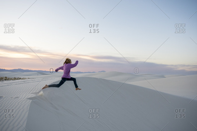 Side view of girl jumping off sand dune in White Sands National Monument, Alamogordo, New Mexico, USA