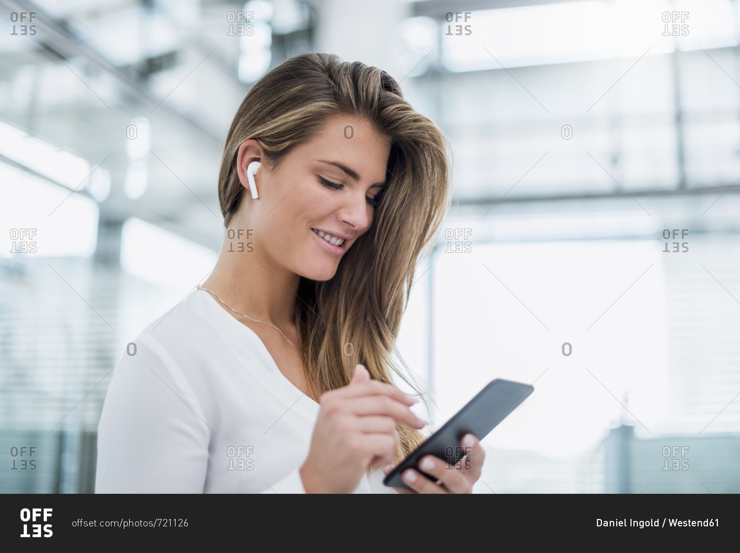 Smiling young woman wearing in-ear phone using cell phone