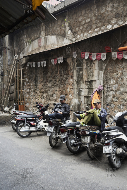 Hanoi, Vietnam - February 28, 2018: Senior Vietnamese workers resting sitting on a motorbike while using technology