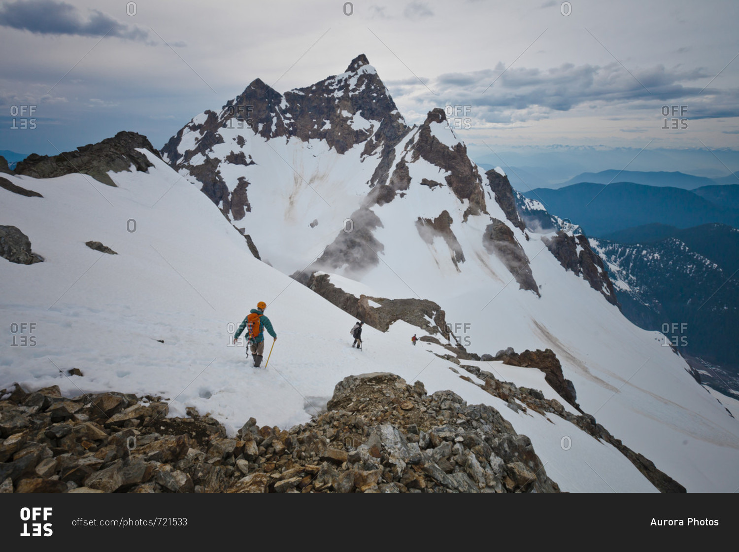 Distant view of three adventurous mountain climbers climbing Foley Peak, North Cascade Mountain Range, Chilliwack, British Columbia, Canada