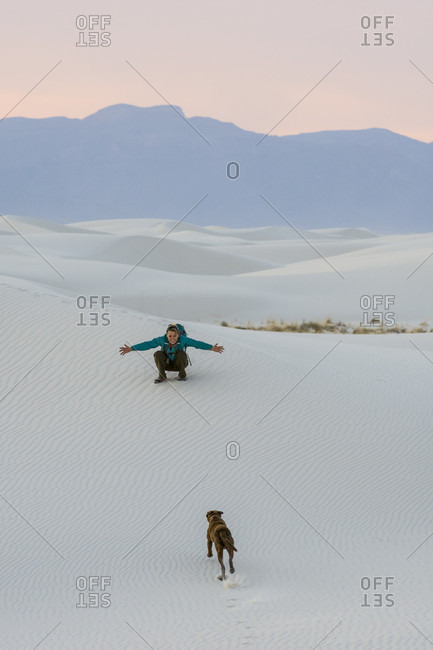 Woman playing with dog while hiking in desert of White Sands National Monument, Alamogordo, New Mexico, USA