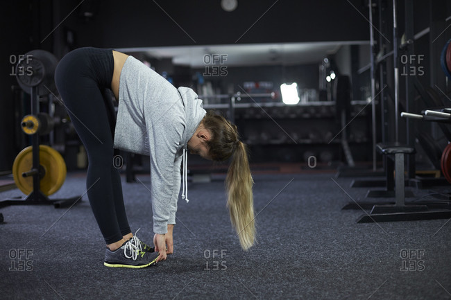 Side view shot of woman in sportswear doing forward bend exercise in gym