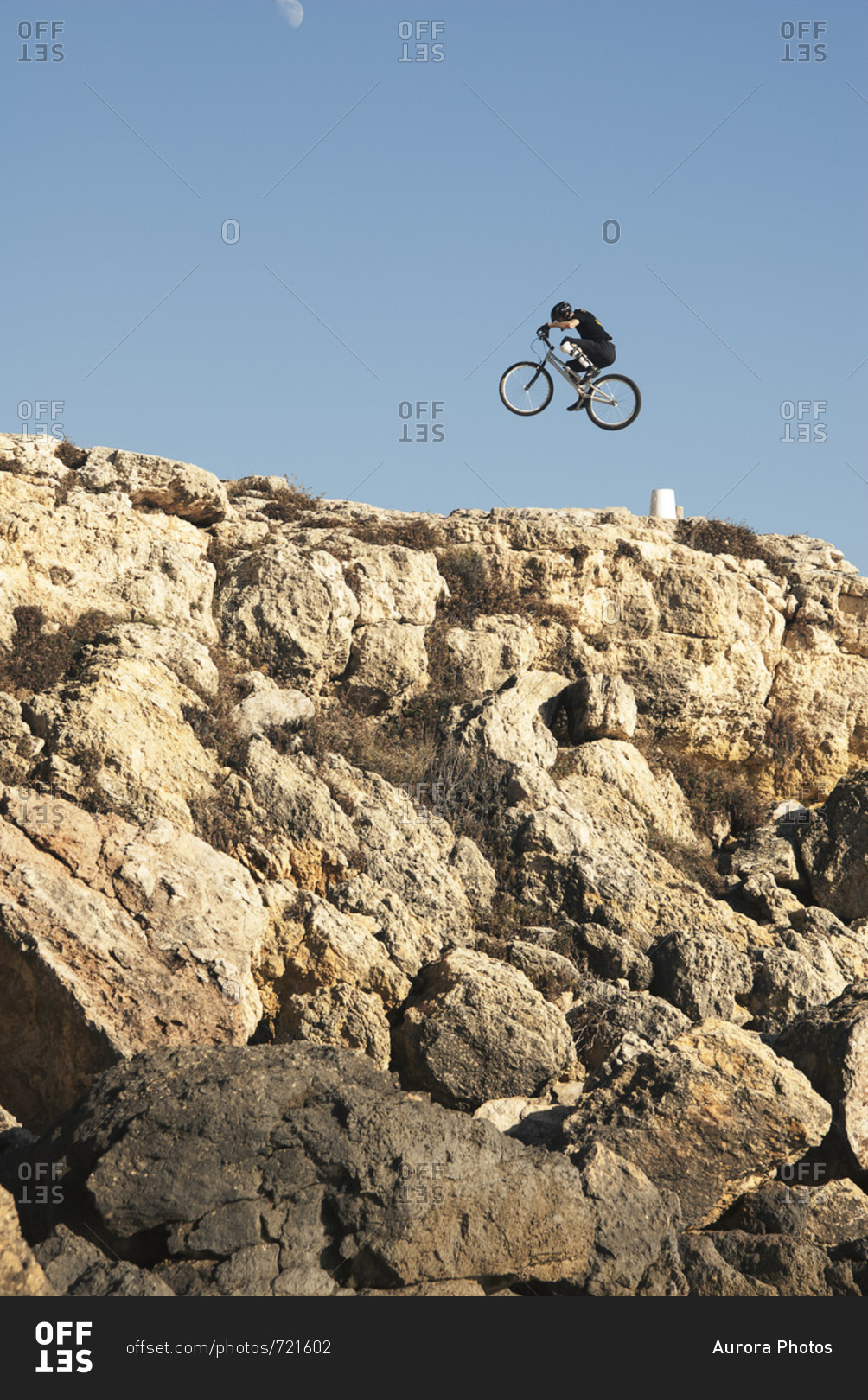 Side view of adventurous mountain biker in mid-air over rocky terrain under clear sky