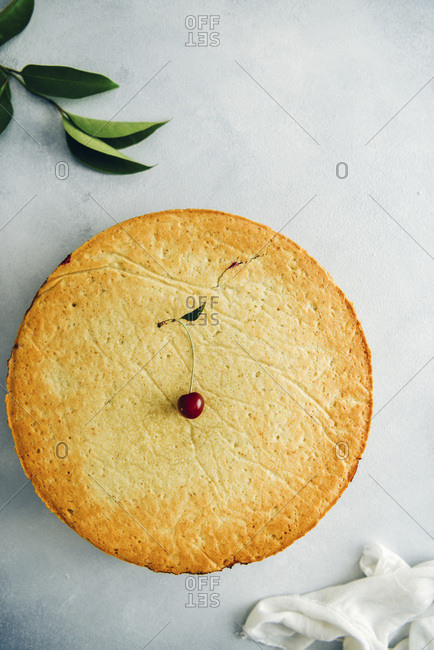 Cherry pie topped with a cherry on grey background photographed from top view Green leaves and white linen accompany
