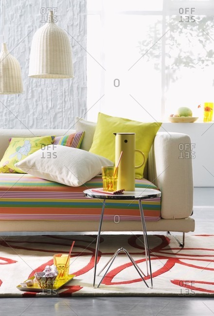 Sofa with striped upholstery and scatter cushions, small side table and wicker pendant lamps
