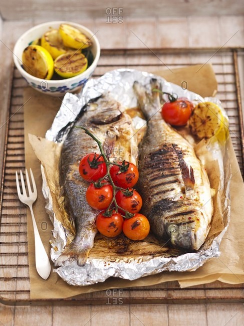 Grilled fish with tomatoes and lemons in aluminium foil on a grill rack