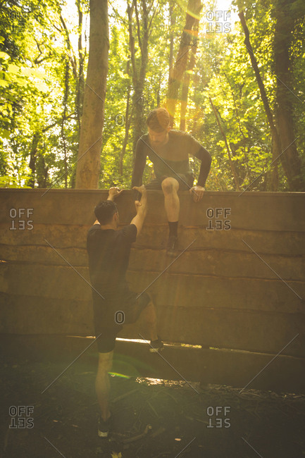 Fit man assisting his teammate to climb a wooden wall at boot camp