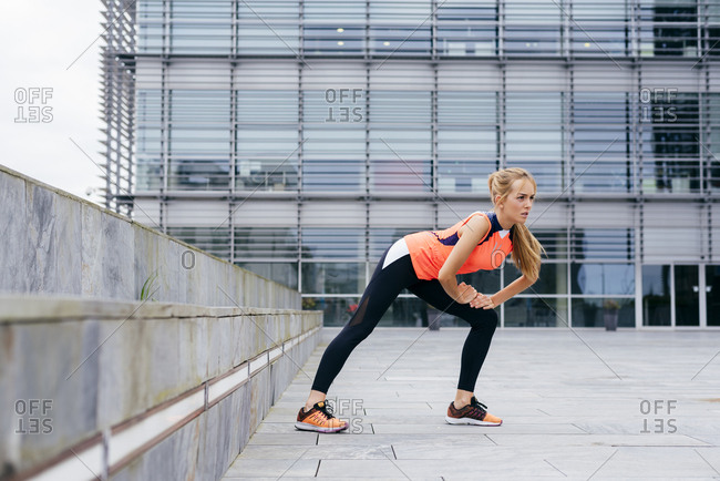 Pretty blonde girl doing stretching on the street before running