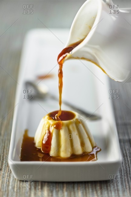 Orange and caramel sauce being poured over panna cotta