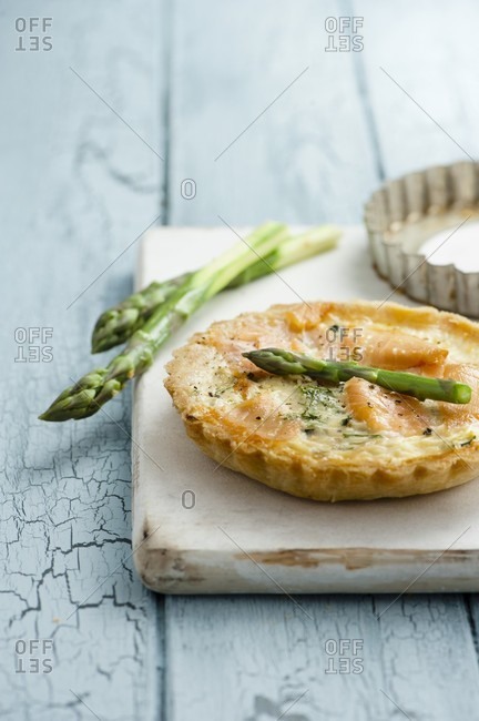 Asparagus and smoked salmon tartlets with asparagus spears on white chopping board