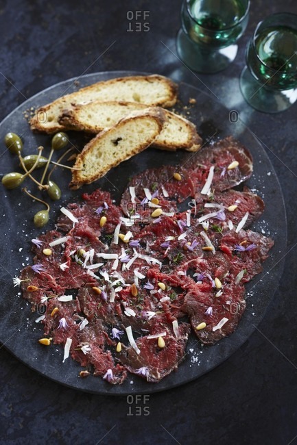 Beef carpaccio with pine nuts, grated cheese, edible flowers, capers and bread