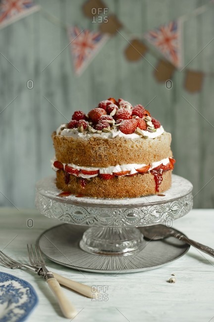 A whole Victoria sponge cake with cream, strawberries, raspberries and pistachios on a cake stand