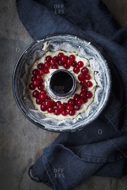 Cake mixture with redcurrants in a Bundt cake tin on a dark wooden surface with a grey cloth