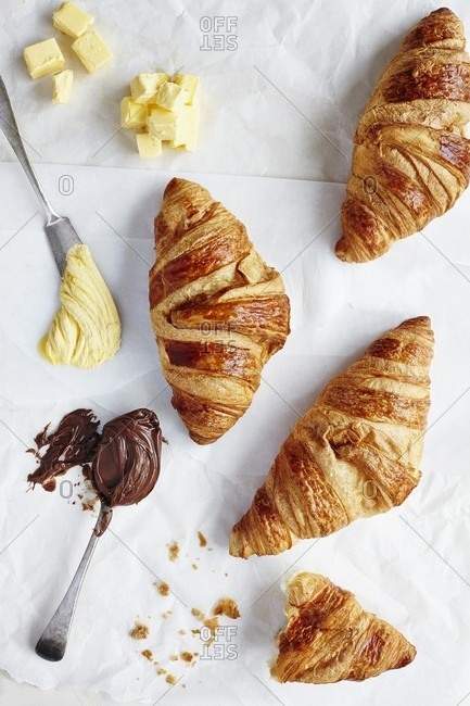 Croissants next to butter and chocolate spread on a spoon and a knife