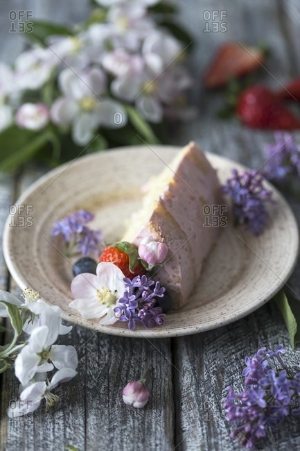 A slice of butter cream cake on a plate decorated with flowers and berries