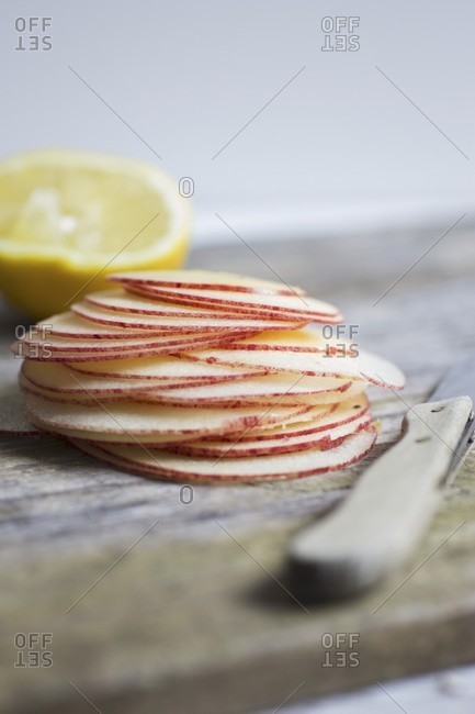 A stack of fine apple slices with a knife and a lemon