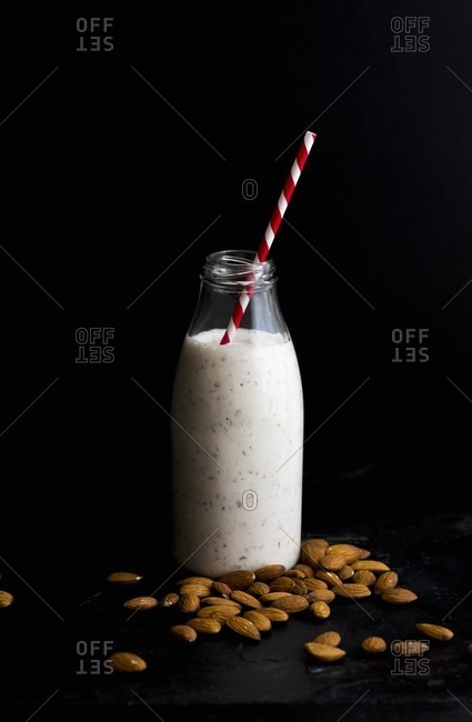 A bottle of almond milk and almond is on a black surface