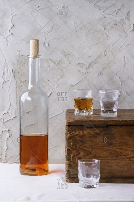 A bottle of rum and three glasses on a wooden chest in front of a plastered wall