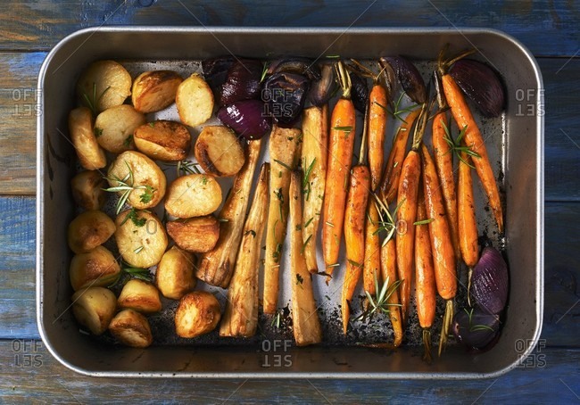 Roasted root vegetables and red onions in a roasting tin