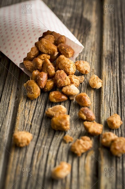 Homemade roasted almonds with a paper bag on a wooden surface