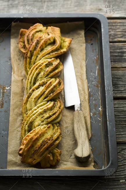 A plaited pesto loaf on a baking tray with a knife