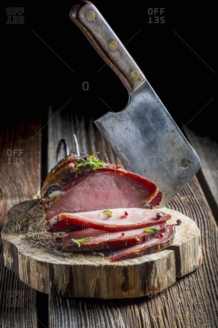 Smoked ham and a meat cleaver on a tree stump
