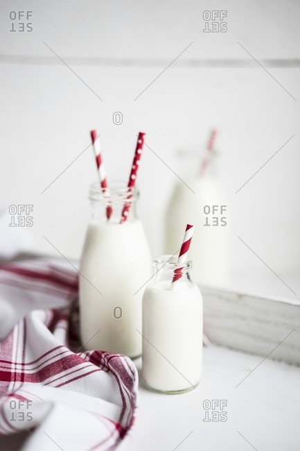 Bottles of milk with red-and-white striped straws on a white wooden surface