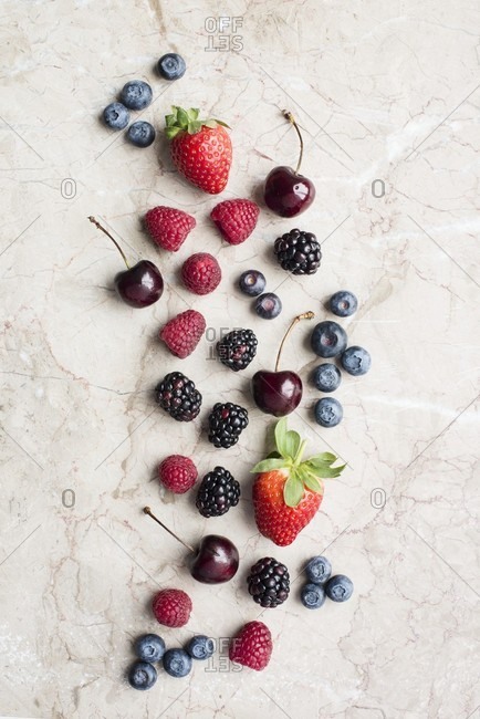 Various fresh berries and cherries on a stone surface