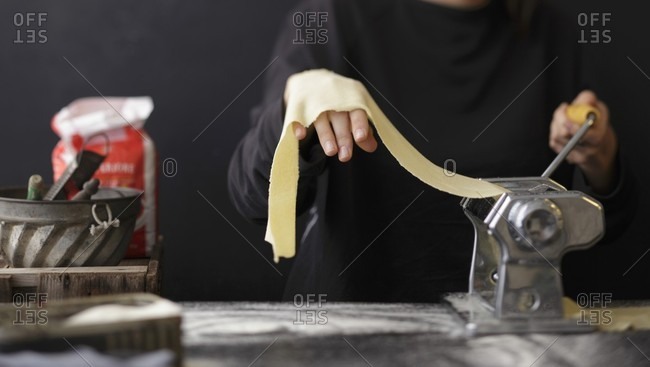 Fresh pasta dough being turned through a pasta machine