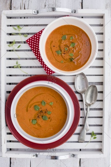 Two bowls of cream of tomato soup with fresh basil on a wooden tray