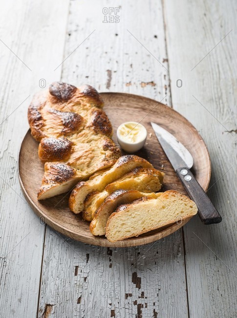 A braided yeast loaf, butter and a knife on a wooden plate