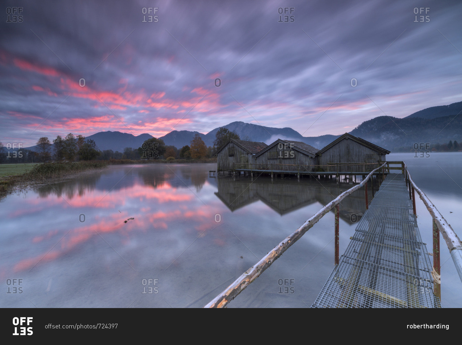 Purple sky at sunset and wooden huts are reflected in the clear water of Kochelsee, Schlehdorf, Bavaria, Germany, Europe