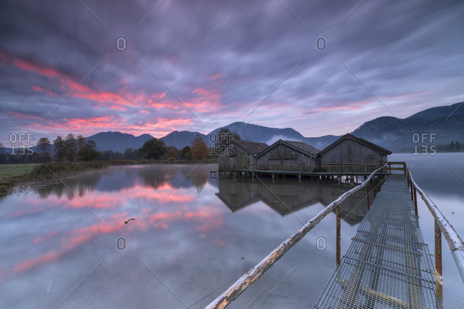 Purple sky at sunset and wooden huts are reflected in the clear water of Kochelsee, Schlehdorf, Bavaria, Germany, Europe