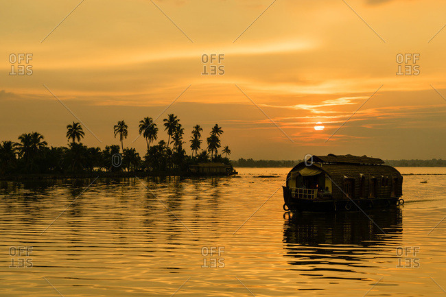 A traditional houseboat moves past the setting sun on the Kerala Backwaters, Kerala, India, Asia