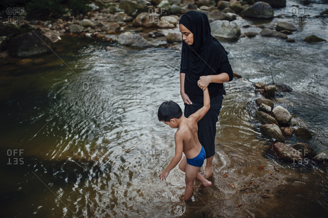 Little boy wading in river holding his mother's hand