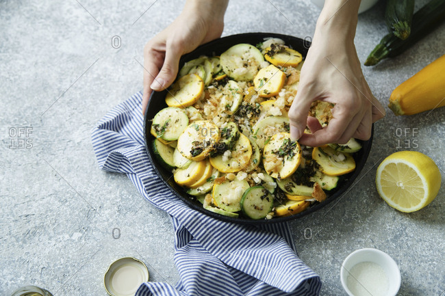 Female hands arranging squash slices, cooking squash and zucchini gratin with herb salsa, cheese and breadcrumbs