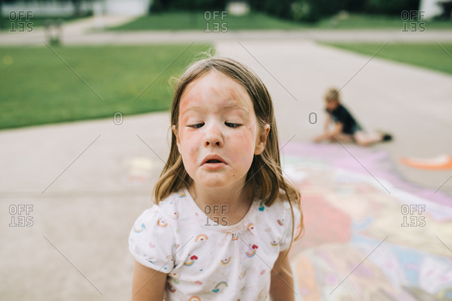 Girl crosses eyes to see chalk dirty face while brother draws with chalk in background