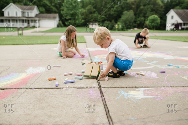 Baby and siblings draw on driveway with chalk